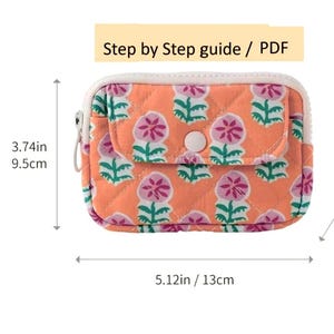 May include: An orange quilted pouch with a floral pattern in pink and green. The pouch has a white zipper and a small pocket with a button closure. It measures 13 cm wide, 9.5 cm high, and 2 cm deep. The text "Step by Step guide / PDF" is at the top.