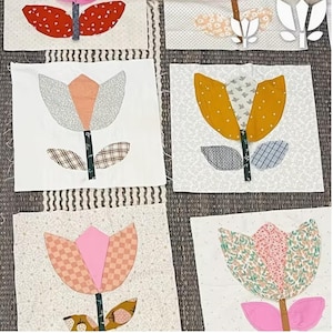 May include: Fabric squares with tulip designs. Each tulip is made from patterned fabrics in red, yellow, pink, and grey, set against a white or patterned background. The stems and leaves are green.