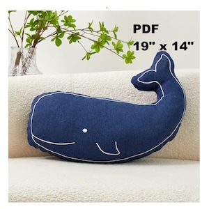 May include: A navy blue whale-shaped cushion with white outline and details. The cushion measures 48 cm by 36 cm. The cushion is on a cream-coloured surface. The text "PDF" is in the upper right corner.