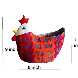 Könnte beinhalten: Ein stofflicher, huhnförmiger Korb, 23 cm hoch, 20 cm breit und 18 cm tief. Der Korb ist hauptsächlich orange mit einem Muster aus blauen und lila Herzen. Er hat einen roten Kamm, einen gelben Schnabel und ein weißes Gesicht.