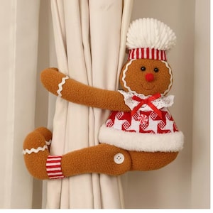 May include: A plush gingerbread person curtain tieback featuring a white chef hat, a red and white patterned top with a red ribbon bow, and white trim. The brown figure has striped cuffs, a red nose, and white wavy accents on the arms.