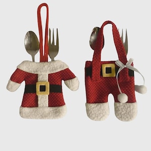 May include: Two Christmas-themed utensil holders shaped like Santa Claus outfits. One is a red jacket with white trim and a black belt. The other is red pants with white trim and a gold buckle. Each holds a spoon and fork.