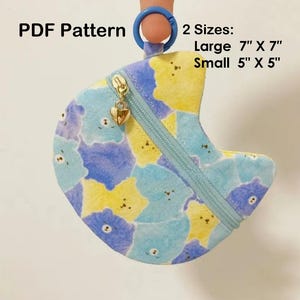 May include: A small, crescent-shaped pouch with a blue zipper and a gold heart charm. The pouch is patterned with blue and yellow bear faces. The text "PDF Pattern" and size details are visible: Large 7" X 7", Small 5" X 5".