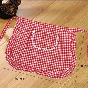 May include: Red and white gingham apron with a pocket and frilled edges. The apron measures 58 cm wide and 41 cm long. The pocket is trimmed with white lace. The apron has long ties.
