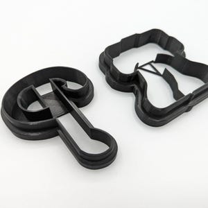 May include: Two black plastic cookie cutters, one shaped like the letter "P" and the other shaped like a baseball cap.
