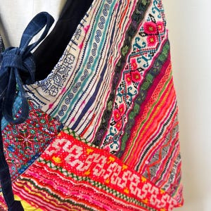 Puede incluir: Bolso de hombro patchwork colorido con una variedad de patrones y texturas. El bolso presenta una mezcla de colores vibrantes, incluyendo rojo, rosa, azul y amarillo, y est&aacute; acentuado con un cierre de lazo azul oscuro.