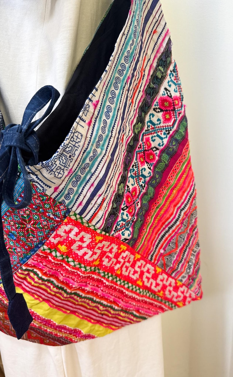 Puede incluir: Bolso de hombro patchwork colorido con una variedad de patrones y texturas. El bolso presenta una mezcla de colores vibrantes, incluyendo rojo, rosa, azul y amarillo, y est&aacute; acentuado con un cierre de lazo azul oscuro.