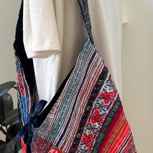 Puede incluir: Un bolso de hombro de patchwork colorido con una correa estampada. El bolso presenta una variedad de telas vibrantes en rojo, rosa, azul y verde, con dise&ntilde;os bordados y a rayas. La correa es azul oscuro con un patr&oacute;n repetitivo.