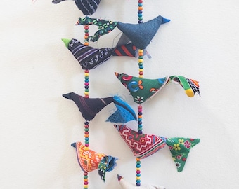 May include: A colorful, handmade bird mobile with fabric birds in various patterns and colors, strung on beaded strands. The birds feature red, blue, green, and patterned fabrics, creating a vibrant, decorative piece.