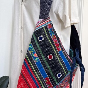 Puede incluir: Bolso de hombro patchwork colorido con una correa estampada. El bolso presenta una variedad de telas vibrantes en rojo, azul, negro y amarillo, con dise&ntilde;os geom&eacute;tricos y florales. La correa es azul oscuro con un patr&oacute;n repetitivo.