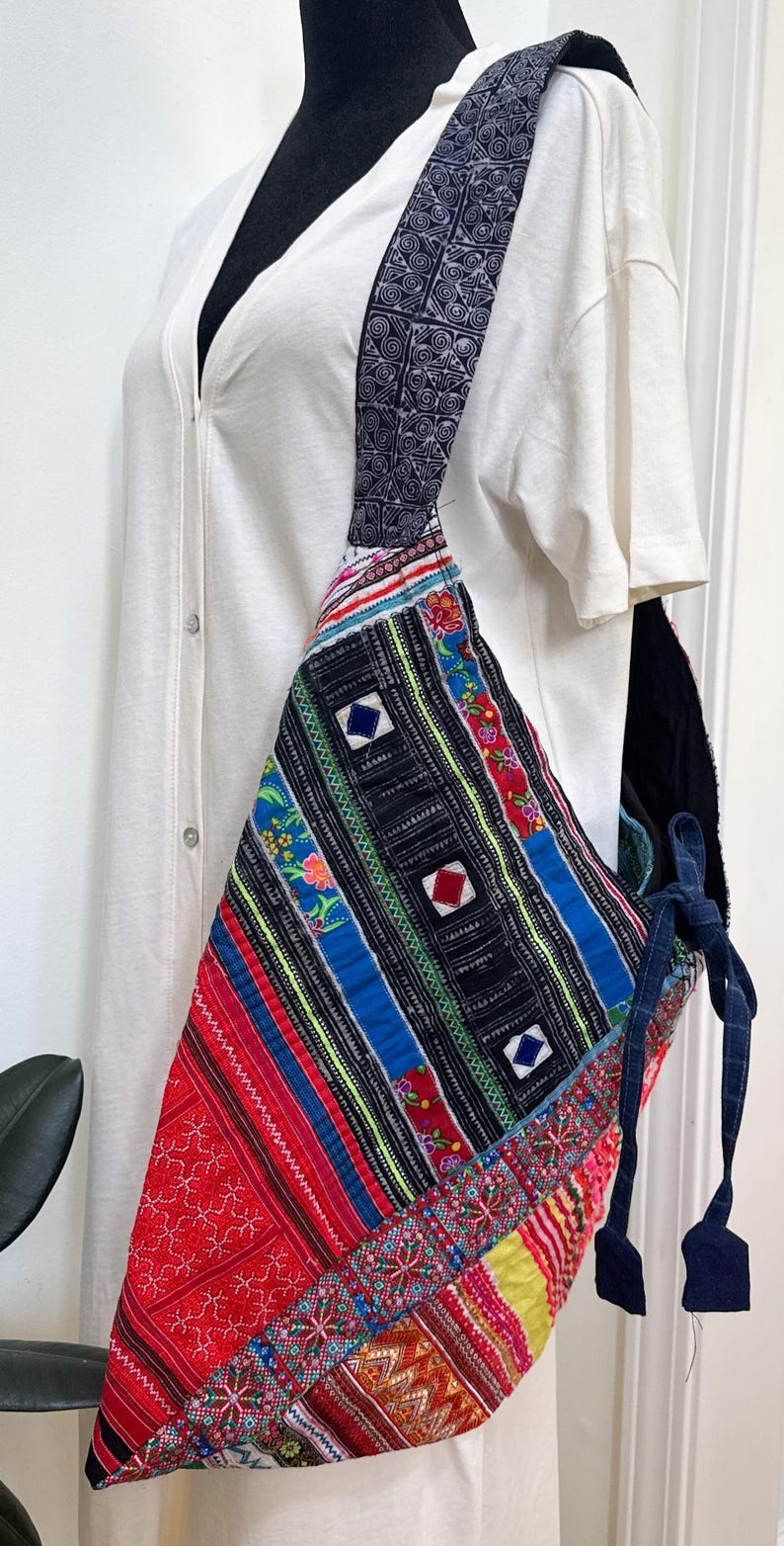 Puede incluir: Bolso de hombro patchwork colorido con una correa estampada. El bolso presenta una variedad de telas vibrantes en rojo, azul, negro y amarillo, con dise&ntilde;os geom&eacute;tricos y florales. La correa es azul oscuro con un patr&oacute;n repetitivo.