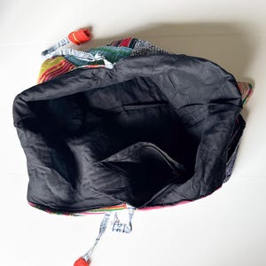 Puede incluir: Un bolso tote grande con un interior negro y un exterior de patchwork colorido. El bolso presenta una variedad de patrones de tela, incluyendo rojo, azul, verde y amarillo. Se aprecia un peque&ntilde;o detalle de ganchillo rojo.