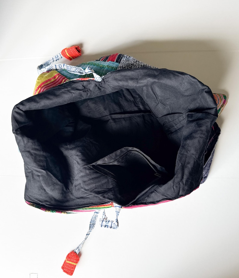 Puede incluir: Un bolso tote grande con un interior negro y un exterior de patchwork colorido. El bolso presenta una variedad de patrones de tela, incluyendo rojo, azul, verde y amarillo. Se aprecia un peque&ntilde;o detalle de ganchillo rojo.