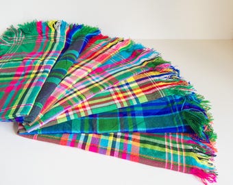 Puede incluir: Una colección de bufandas a cuadros coloridas con bordes con flecos. Las bufandas muestran una variedad de colores vibrantes, incluyendo verde, azul, rosa, amarillo y rojo. El patrón de cuadros es visible en cada bufanda.