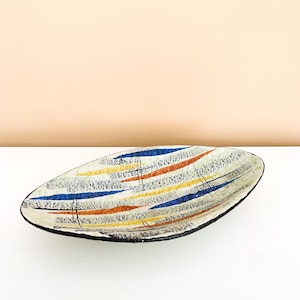 May include: Oval ceramic dish with a white base and a black rim. The dish is decorated with horizontal stripes in blue, orange, and yellow. The dish has a mid-century modern design.
