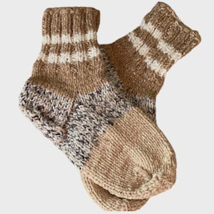 May include: A pair of hand-knitted socks in shades of brown, beige, and white. The socks feature a striped pattern at the cuff and a textured knit design throughout. The socks are made of a soft, warm material.