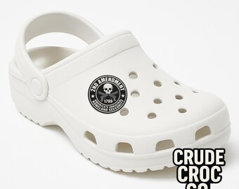May include: White clog-style shoe with a pivoting heel strap. Features a circular emblem with a skull, crossed rifles, and the text "2ND AMENDMENT AMERICA'S ORIGINAL HOMELAND SECURITY 1789." The text "CRUDE CROC CO." is printed on the side.
