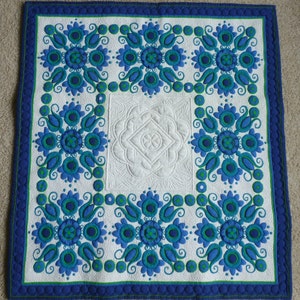 May include: A white quilt with a blue and green floral pattern. The quilt is quilted with a diamond pattern in the center and a circle pattern around the edges.