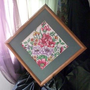May include: A framed floral print with a green background. The print features a bouquet of pink, red, and purple flowers with green leaves on a white background.