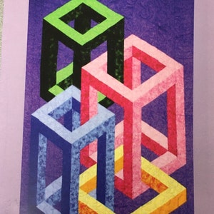 May include: A colorful geometric pattern with four interlocking cubes in shades of green, black, pink, blue, yellow, and orange. The cubes are arranged in a complex, three-dimensional design against a purple background. The text "Boxed" is printed at the top of the image. The text "Finished Size 50 x 57" is printed at the bottom of the image.