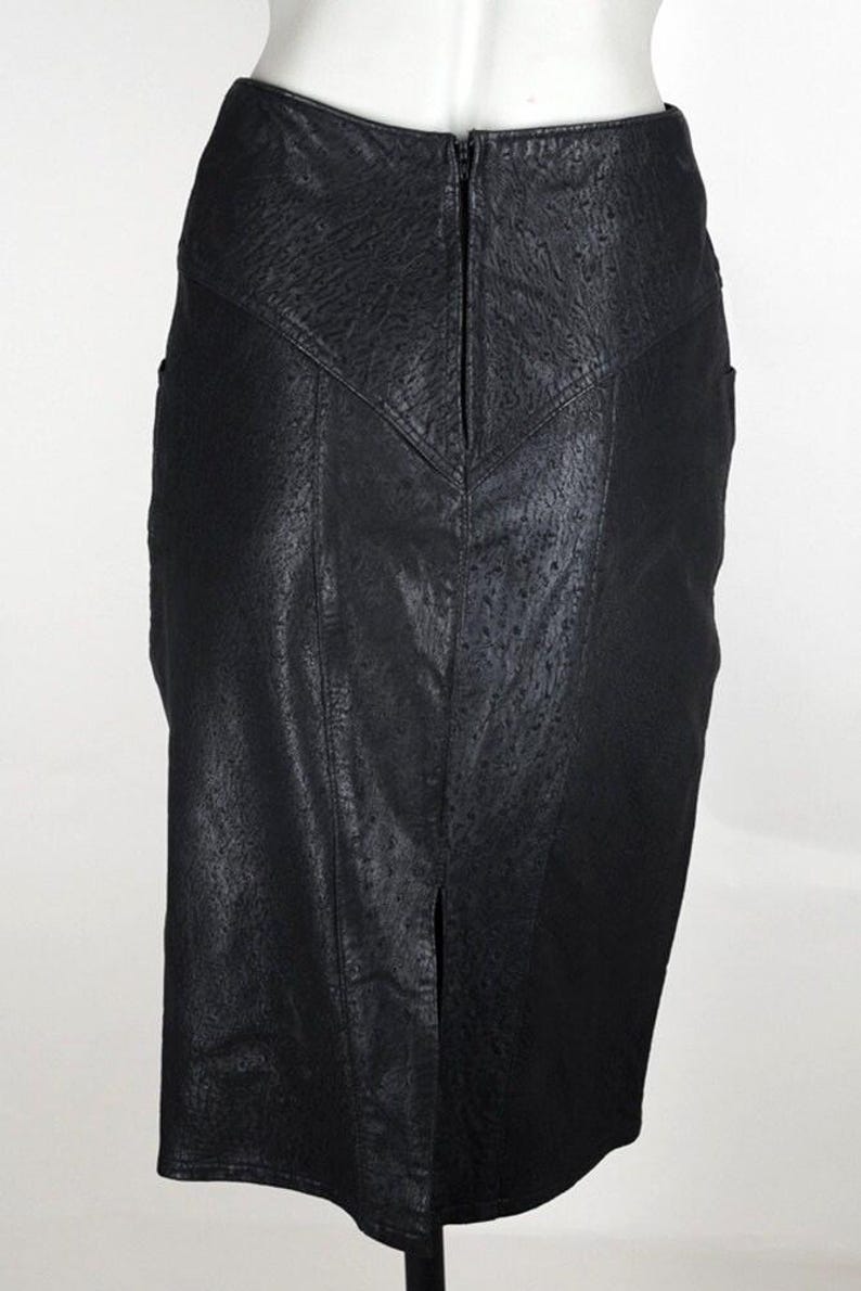 May include: A black pencil skirt with a textured, leather-like appearance. The skirt features a front slit and a zipper closure at the back. The design includes a V-shaped yoke at the waist and vertical panels.