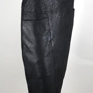 May include: A black pencil skirt with a textured surface and two front pockets. The skirt is displayed on a mannequin and has a knee-length hemline. The material appears to be leather or a leather-like fabric.