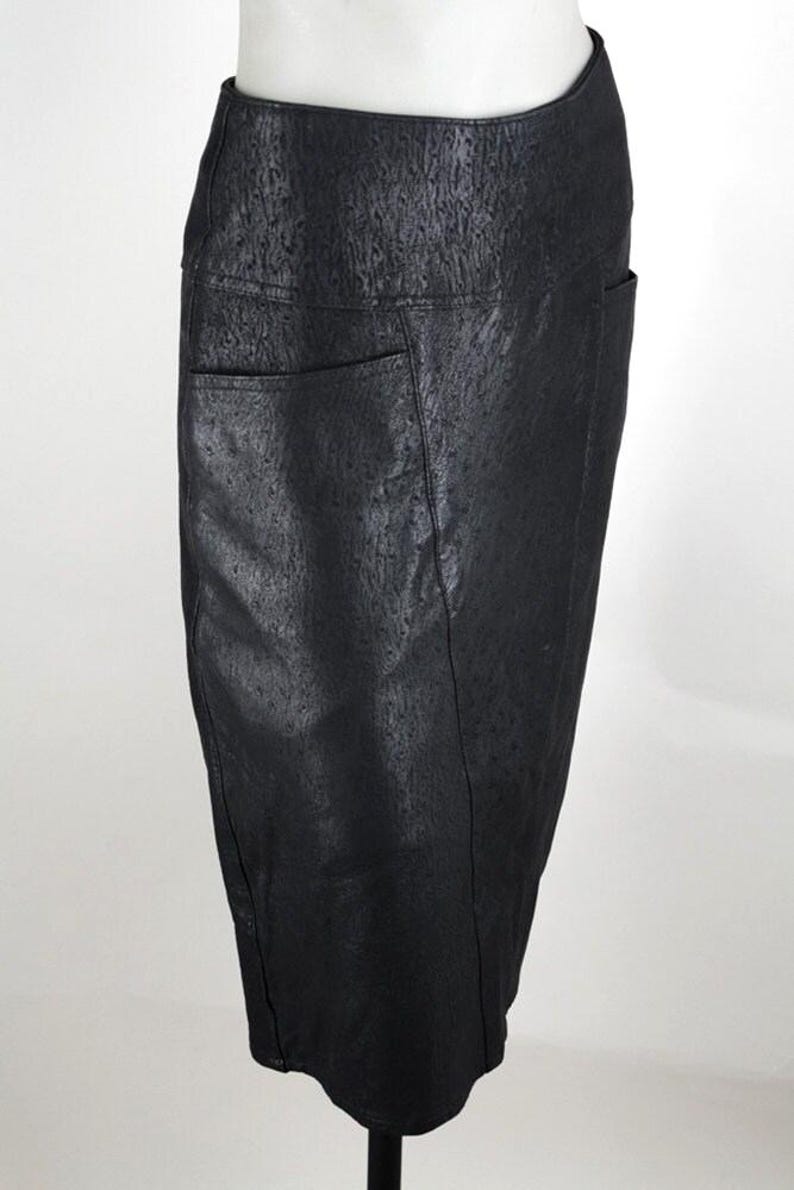 May include: A black pencil skirt with a textured surface and two front pockets. The skirt is displayed on a mannequin and has a knee-length hemline. The material appears to be leather or a leather-like fabric.