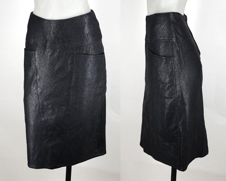May include: A black, knee-length skirt with a textured surface and two front pockets. The skirt is displayed on a mannequin, showcasing its tailored fit and design. The skirt's material appears to be leather or a leather-like fabric.