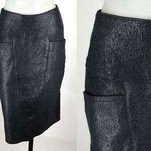 May include: A black pencil skirt with a textured, leather-like appearance. The skirt features two front pockets and a fitted silhouette. The fabric has a subtle, mottled pattern, adding visual interest to the garment.