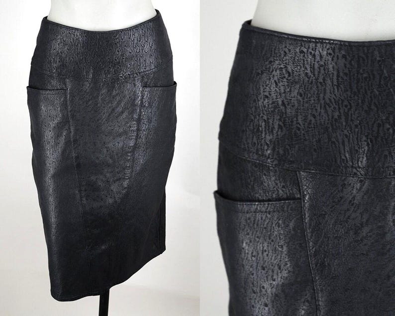 May include: A black pencil skirt with a textured, leather-like appearance. The skirt features two front pockets and a fitted silhouette. The fabric has a subtle, mottled pattern, adding visual interest to the garment.