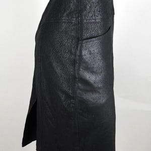May include: A black, knee-length skirt with a textured surface and a high waist. The skirt features a side slit and a single pocket. The garment is displayed on a mannequin against a white background.