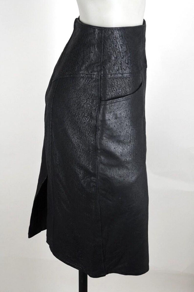 May include: A black, knee-length skirt with a textured surface and a high waist. The skirt features a side slit and a single pocket. The garment is displayed on a mannequin against a white background.
