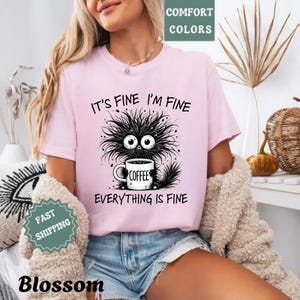a woman wearing a pink shirt that says it's fine i'm fine