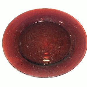 May include: A dark red glass plate with a smooth, slightly textured surface. The plate is round and has a slightly raised rim.