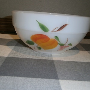 May include: White ceramic bowl with a hand-painted design of fruit, including peaches and leaves. The bowl has a slightly rounded shape and a smooth, glossy finish.