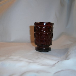 May include: A dark red glass vase with a geometric pattern. The vase has a wide base and a narrow opening.