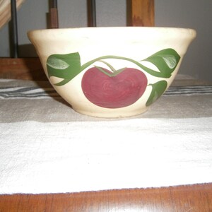 May include: A white ceramic mixing bowl with a green and red apple design. The bowl is decorated with a single red apple with green leaves.