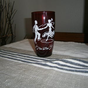 May include: A dark red translucent glass tumbler featuring a white graphic of two figures square dancing. The design includes the text "Do Si Do" written in a cursive script below the dancers, accompanied by small white musical note symbols.