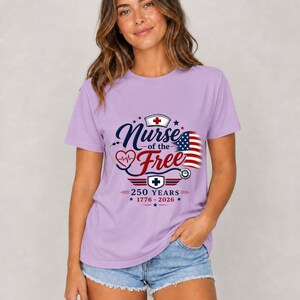 May include: A lilac-colored t-shirt with the text "Nurse of the Free" in navy blue script, featuring a heart, stethoscope, and American flag design. The shirt also includes the text "250 YEARS 1776-2026".