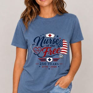 May include: Blue t-shirt with a graphic that reads "Nurse of the Free" in a patriotic design. The design includes a nurse's cap, stethoscope, and the American flag. The text "250 Years 1776-2026" is also included.