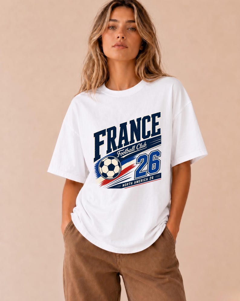 May include: A white short-sleeved t-shirt featuring a graphic print with the text FRANCE, Football Club, and the number 26. The design includes a football and red, white, and blue stripes with the additional text North America 26.