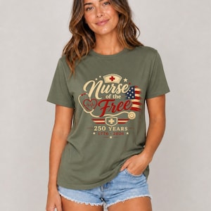 May include: Olive green t-shirt with the text "Nurse of the Free" in a vintage design, featuring a stethoscope, a nurse's cap, and an American flag. The shirt also includes the text "250 YEARS 1776-2026".