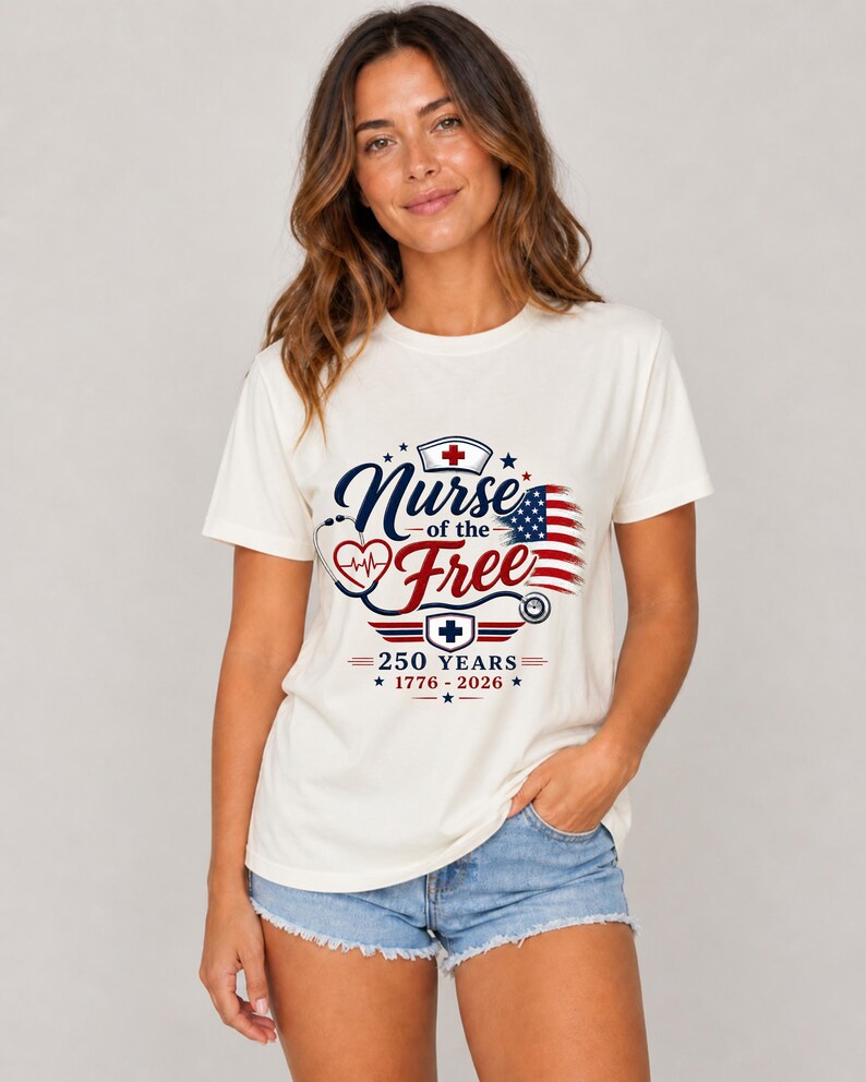 May include: Cream-colored t-shirt featuring the text "Nurse of the Free" in navy blue script, with a red heart and stethoscope design. The design includes an American flag and the text "250 YEARS 1776-2026". The model is wearing denim shorts.