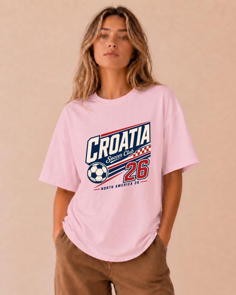 K&ouml;nnte beinhalten: Ein hellrosa T-Shirt mit kurzen &Auml;rmeln und einem Grafikdesign, das den Text CROATIA Soccer Club, die Zahl 26, einen Fu&szlig;ball und ein rot-wei&szlig;es Karomuster zeigt. Der Text NORTH AMERICA 26 ist in kleineren Buchstaben unter der Grafik gedruckt.