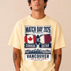 May include: A light yellow t-shirt featuring a graphic for the 2026 Match Day in North America. The design includes the flags of Canada and Qatar, the city of Vancouver, and the date and time of the match.