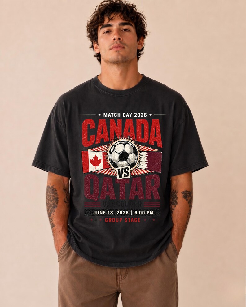 May include: Black t-shirt with a soccer-themed graphic. The design features the text "CANADA" and "QATAR" with a soccer ball in the center. Additional text includes "MATCH DAY 2026", "VANCOUVER", "JUNE 18, 2026 | 6:00 PM", and "GROUP STAGE".