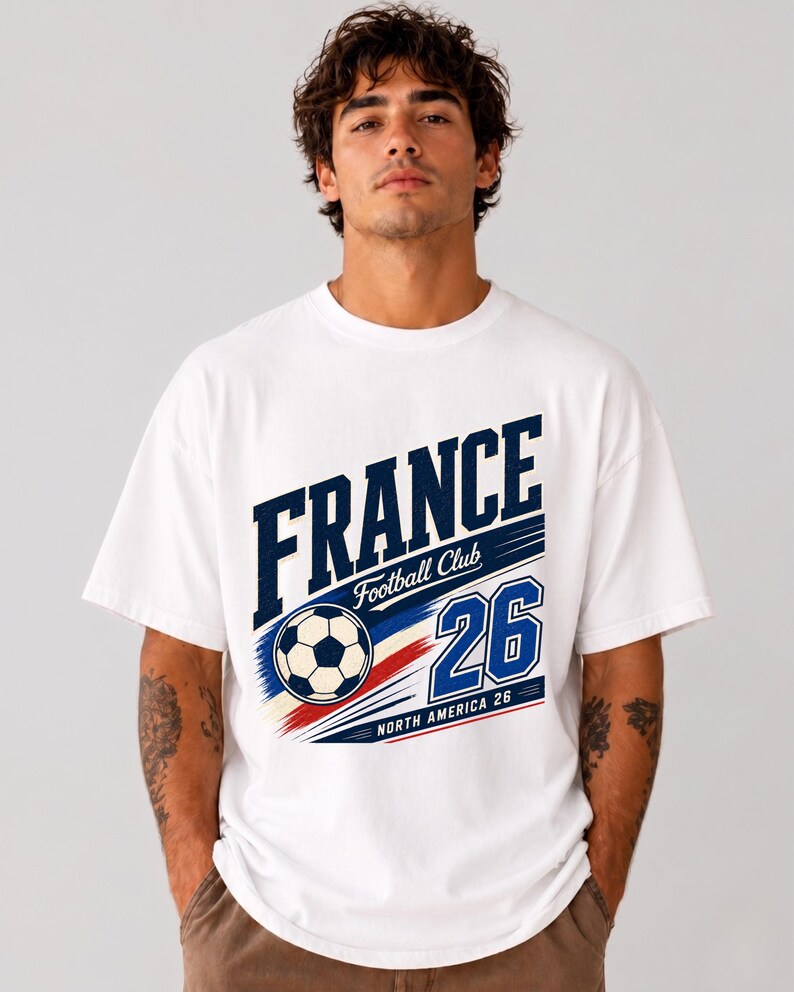 May include: A white short-sleeve t-shirt featuring a graphic print with the text FRANCE, Football Club, and 26. The design includes a football, blue and red brush strokes, and the text NORTH AMERICA 26 in a bold, athletic font style.