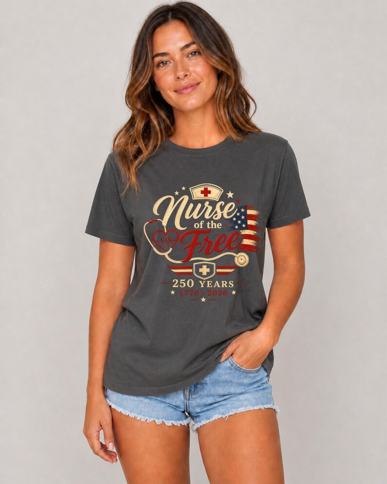 May include: Dark gray t-shirt with the text "Nurse of the Free" in a vintage design, featuring a stethoscope, cross, and American flag. The shirt also includes the text "250 Years 1776-2026".