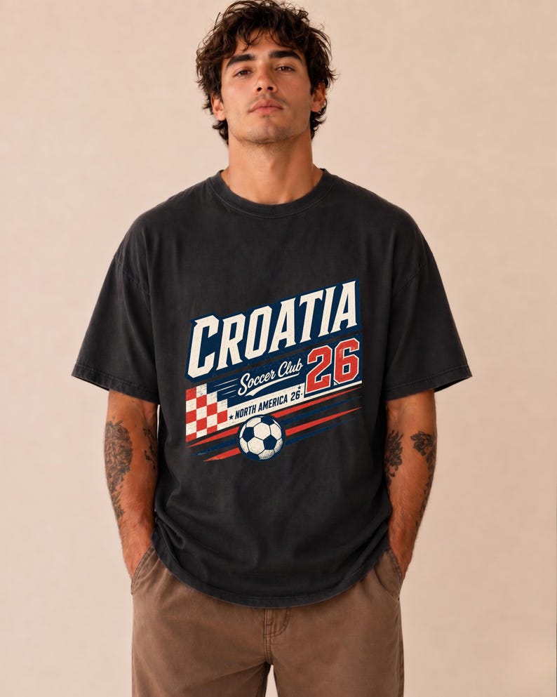 以下が含まれることがあります： CROATIA Soccer Club 26 NORTH AMERICA 26と書かれたグラフィックプリントが施されたチャコールグレーの半袖Tシャツ。デザインには、赤と白の市松模様の正方形、サッカーボール、赤と青の水平ストライプが含まれています。