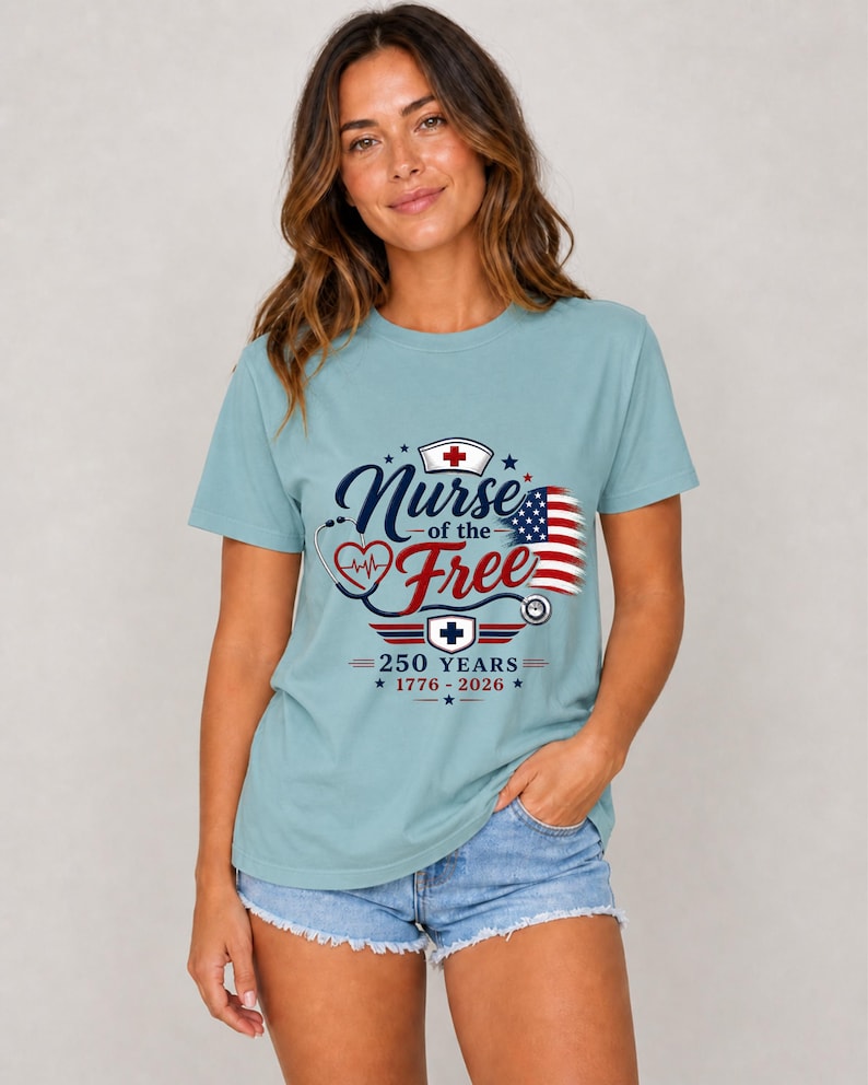 May include: A light blue t-shirt with the text "Nurse of the Free" in navy blue script, featuring a red heart, stethoscope, and American flag design. The shirt also includes the text "250 YEARS 1776-2026".